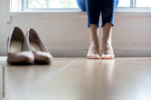 Barefoot woman, focus on feet and shoes in blur. Symbolic image resting the feet after walking with high heel shoes Backlit image.