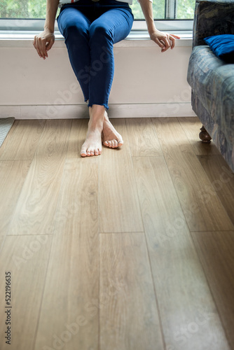 Woman sitting and barefoot relaxing on wooden floor in home environment. Copy space.