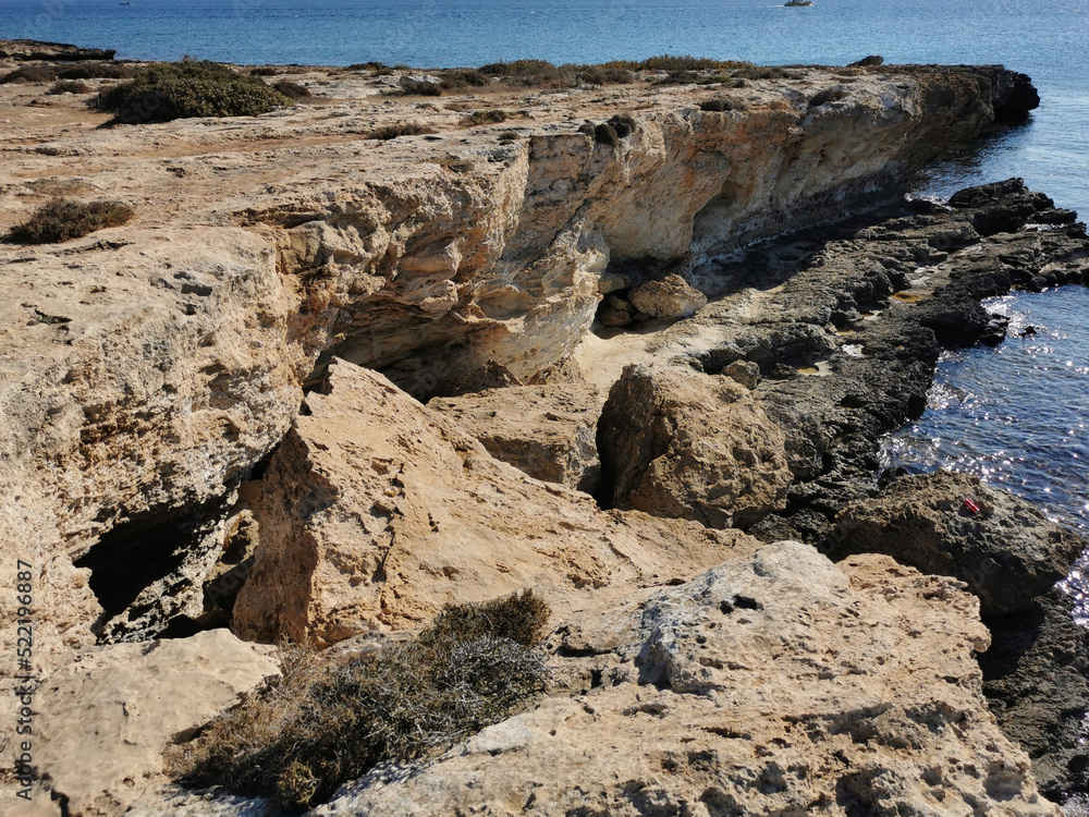 A rocky shore of long-hardened lava, a cliff, the Mediterranean Sea with a boat. A rocky shore of long-hardened lava, a cliff, the Mediterranean Sea with a boat.