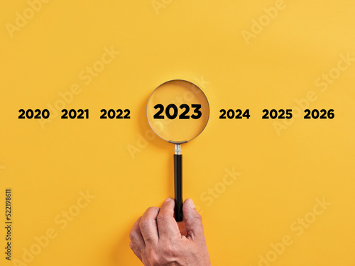 Male hand holds a magnifier focusing on the year 2023. Focus on new business goals, plan and strategy of the year 2023