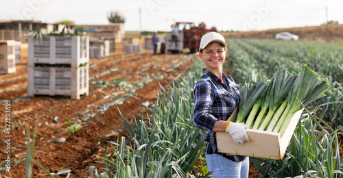 Positive female farmer with a box of leeks in the field photo