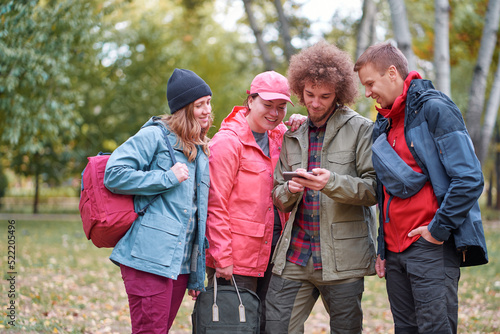 Holidays with friends. Group of young people using smartphone together in the park.