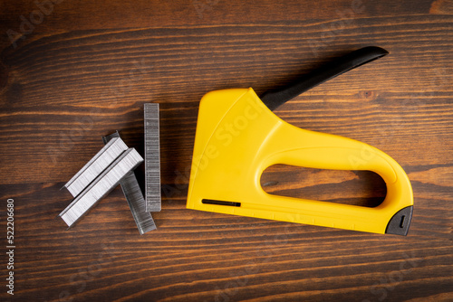 Yellow plastic staple gun and metal staples on wooden background