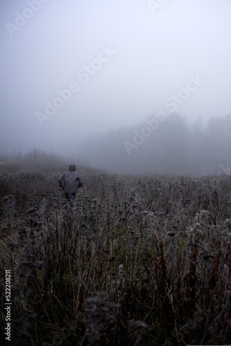 On a foggy gray autumn morning, a man runs into a field © Olesia