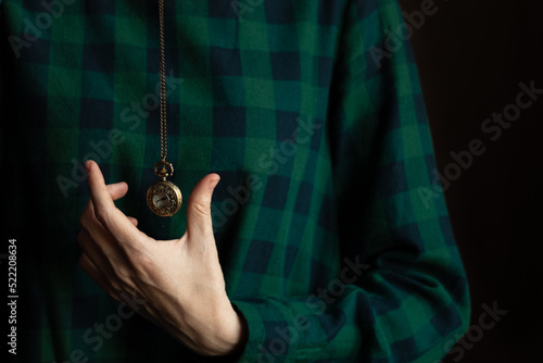 Vintage pocket watch on a chain in hand on a green background