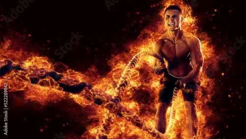 Muscular man working out with battle ropes. Flame background
