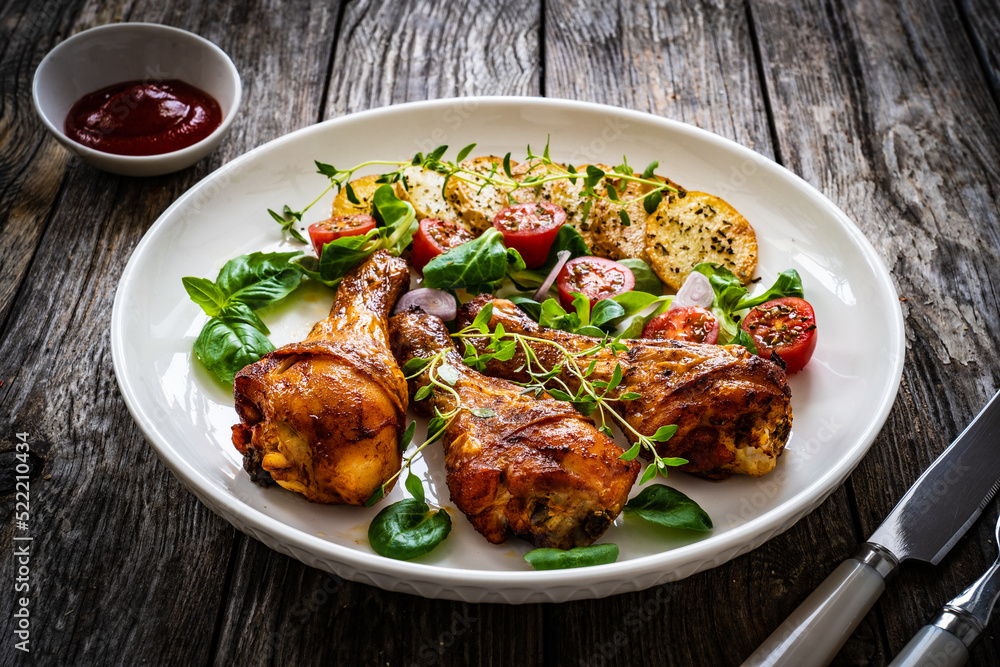 Barbecue chicken drumsticks with fried potato, lettuce and mini tomatoes on wooden table
