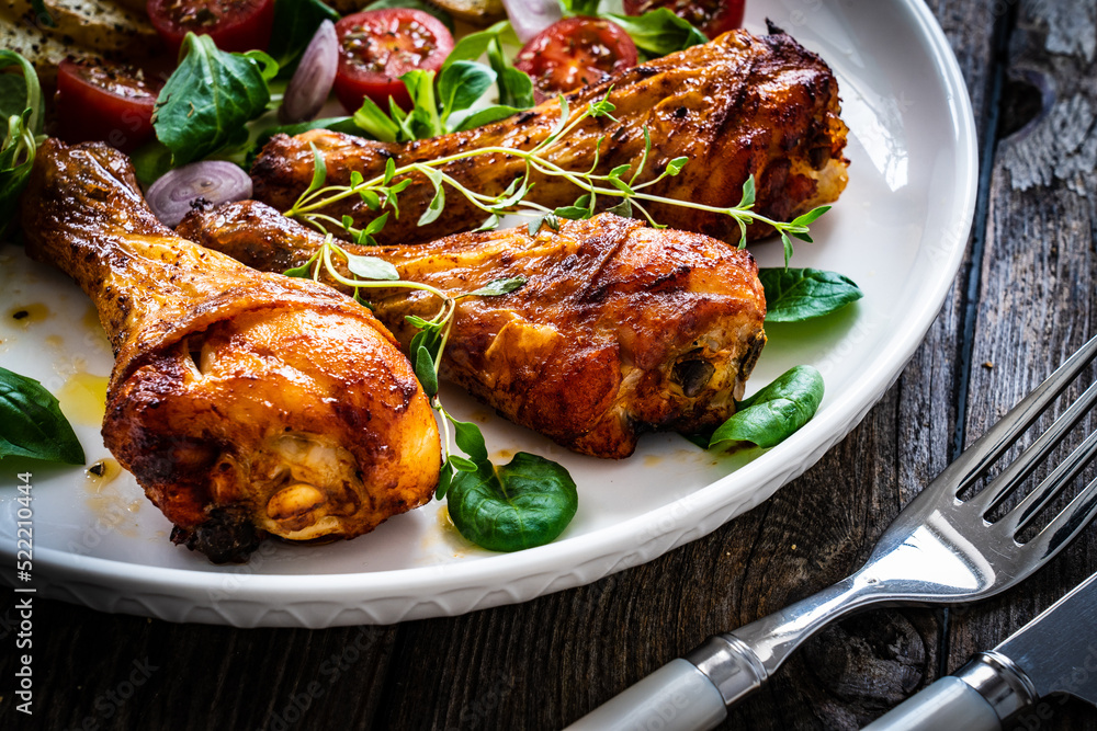 Barbecue chicken drumsticks with fried potato, lettuce and mini tomatoes on wooden table
