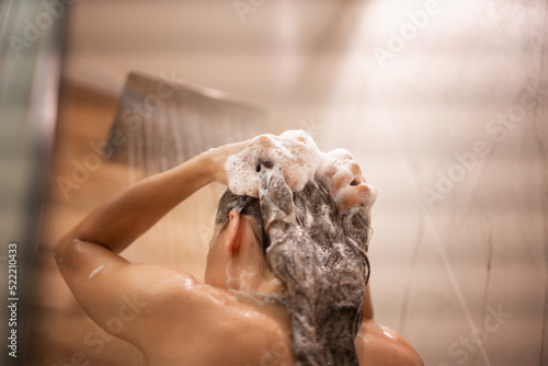 Obraz na plátne Young woman washing her hair and head in the shower, soap suds on her hair