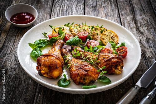 Barbecue chicken drumsticks with fried potato, lettuce and mini tomatoes on wooden table
