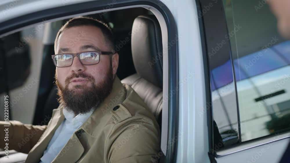 an adult man sits in the salon of a new car, in a dealership. Talented seller, tells about the conditions for purchasing a car. an adult man sits in the salon of a new car, in a dealership. Talented seller, tells about the conditions for purchasing a car.