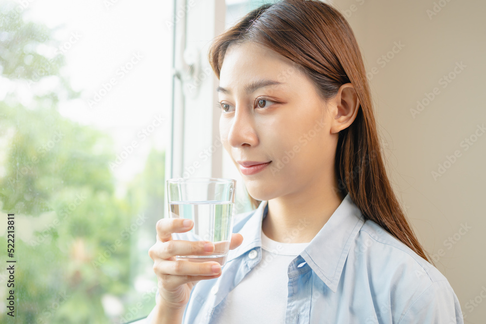 Happy beautiful, asian young woman, girl drinking, sip fresh glass of water for hydration of body, holding transparent glass in her hand, thirsty at home. Health care, healthy lifestyle concept. Happy beautiful, asian young woman, girl drinking, sip fresh glass of water for hydration of body, holding transparent glass in her hand, thirsty at home. Health care, healthy lifestyle concept.