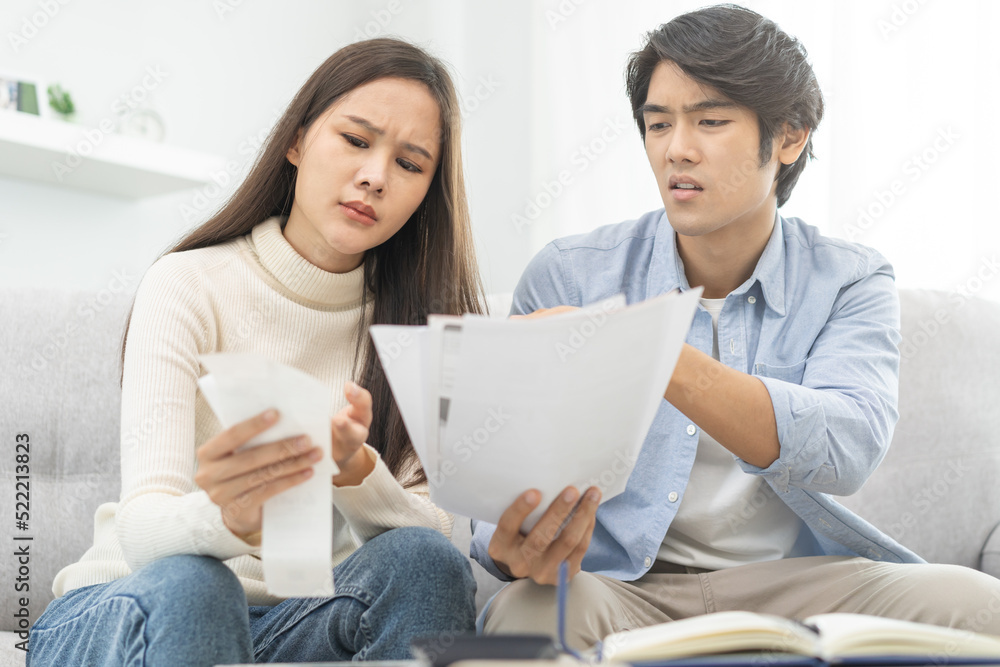 Stressed financial owe asian young couple love hand in holding bills, sitting on sofa together, stressed and confused by calculate expense, mortgage or loan. Debt, bankrupt or bankruptcy people. Stressed financial owe asian young couple love hand in holding bills, sitting on sofa together, stressed and confused by calculate expense, mortgage or loan. Debt, bankrupt or bankruptcy people.