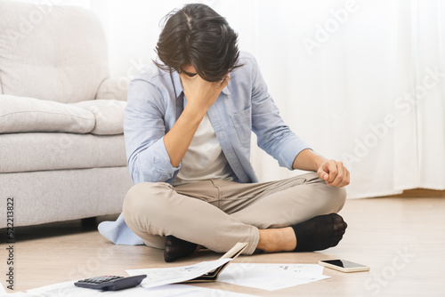 Financial, owe asian man, male sitting on floor home, stressed and confused by calculate expense from invoice or bill, have no money to pay, mortgage or loan. Debt, bankruptcy or bankrupt concept.