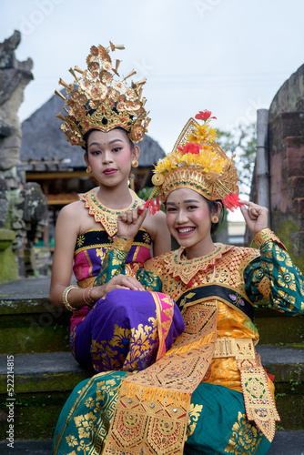 Two young Bali smiling girls make -up dressed in traditional colored costumes inside in the temple.