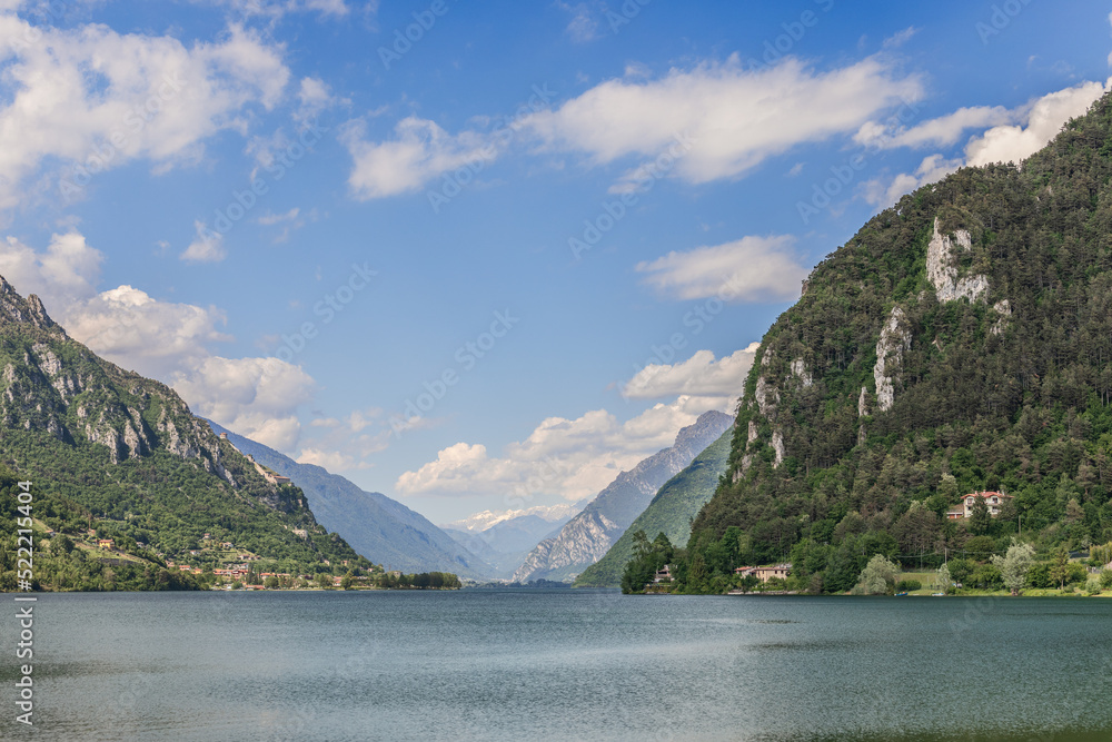 Panorama and perspective of Lombardean unique lake Lago d'Idro framed by wooded cliffs under summer blue sky with few white clouds. Brescia, Italy