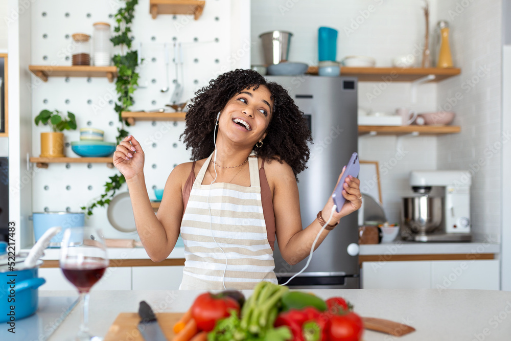 young amazing emotional woman dancing in kitchen indoors at home listening music with headphones cooking.