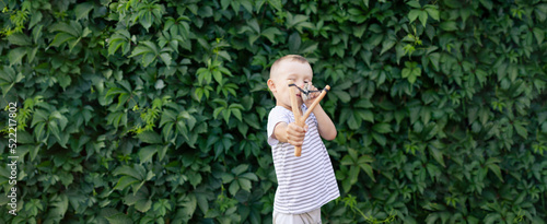 a boy in a T-shirt on the background of a hedge aims a slingshot. banner with space for text