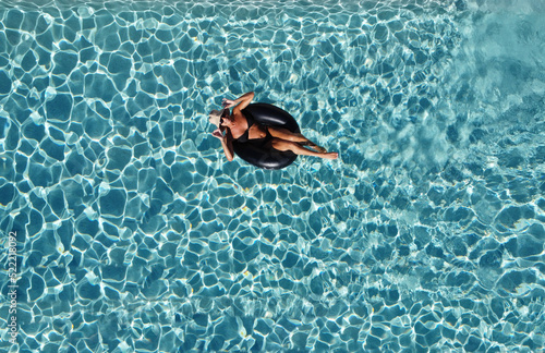 smiling woman in black bikini and hat floating on swimming pool water