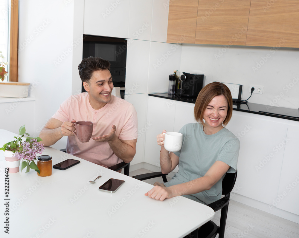 Young happy married couple drinking tea and laughing in the kitchen at home. Leisure time and togetherness concept Young happy married couple drinking tea and laughing in the kitchen at home. Leisure time and togetherness concept