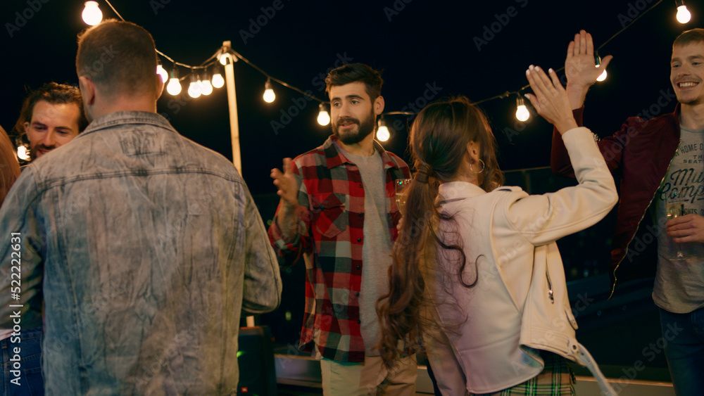 Group of young people have a party on the rooftop of terrace they are drinking some champagne and enjoy the evening smiling large and hugging each other