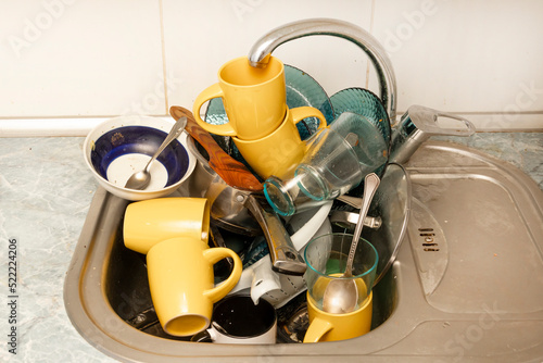 Dirty and unwashed dishes are stacked in the kitchen sink. Unwashed cups, plates, pots, forks and spoons.A mountain of untidy and used dishes.