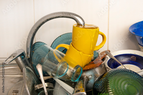 Dirty and unwashed dishes are stacked in the kitchen sink. Unwashed cups, plates, pots, forks and spoons