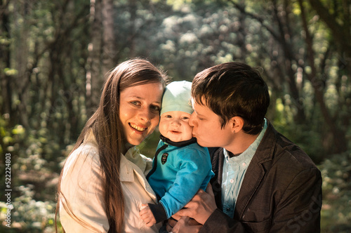 Portrait of a happy young family spending time together in summer nature, on vacation, in nature. Mom and dad hold baby son in their arms and kiss © Anna