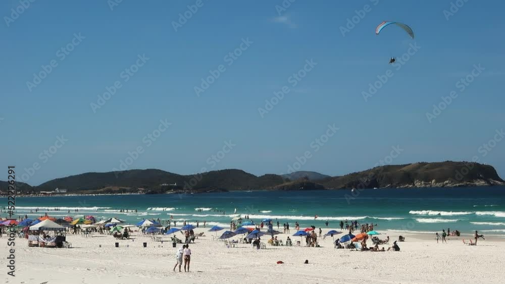 Paramotor flying over crowded beach in Cabo Frio, Brazil, at sunny day. Slow Motion Paramotor flying over crowded beach in Cabo Frio, Brazil, at sunny day. Slow Motion