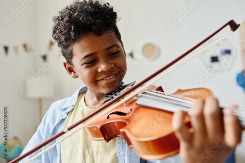Obraz na plátně Smiling African boy playing violin at home during lesson