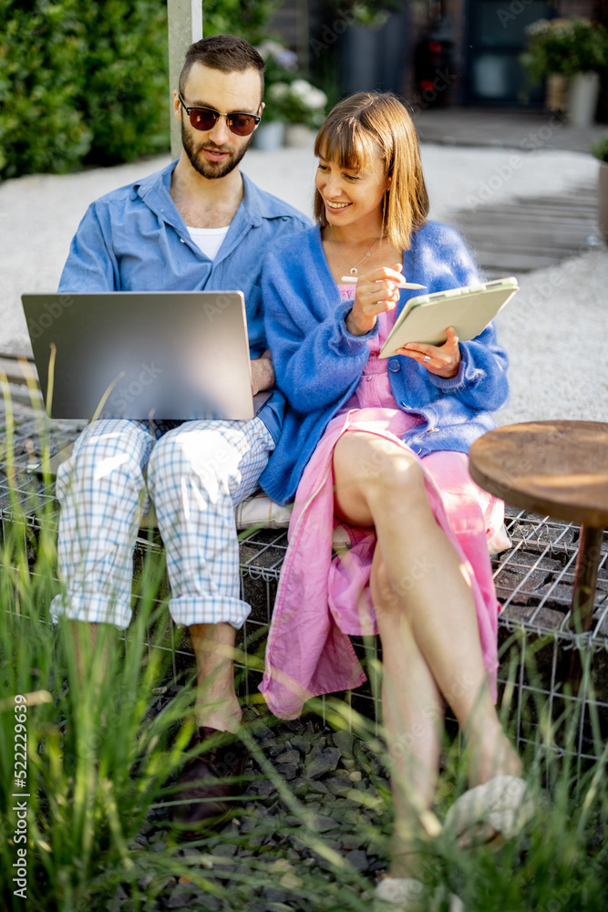 Φωτογραφία Young stylish couple work or spend leisure time with laptop computer and digital tablet on porch of their country house