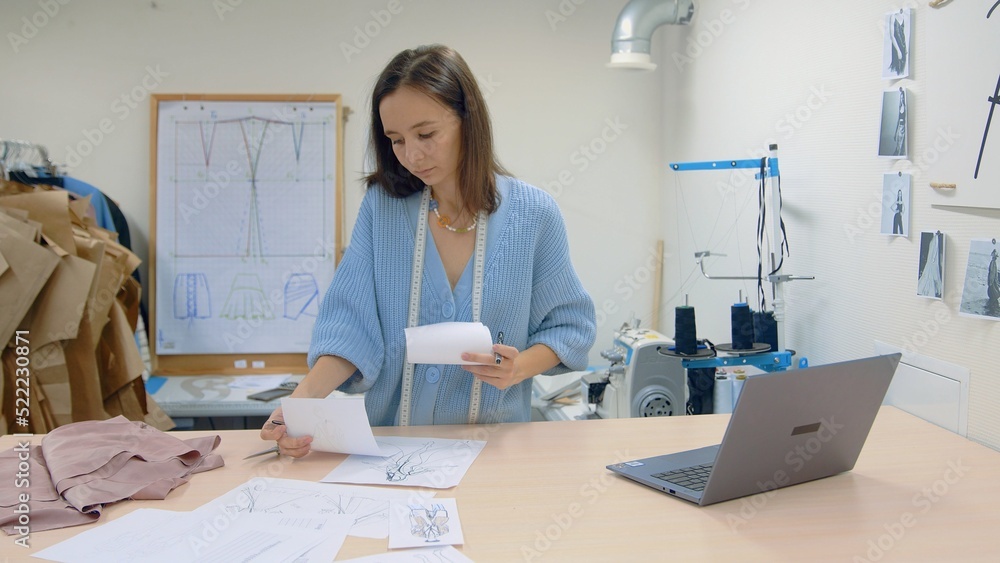 Obraz premium 4K. A young woman working in a clothing store. A fashion designer makes sketches on paper.