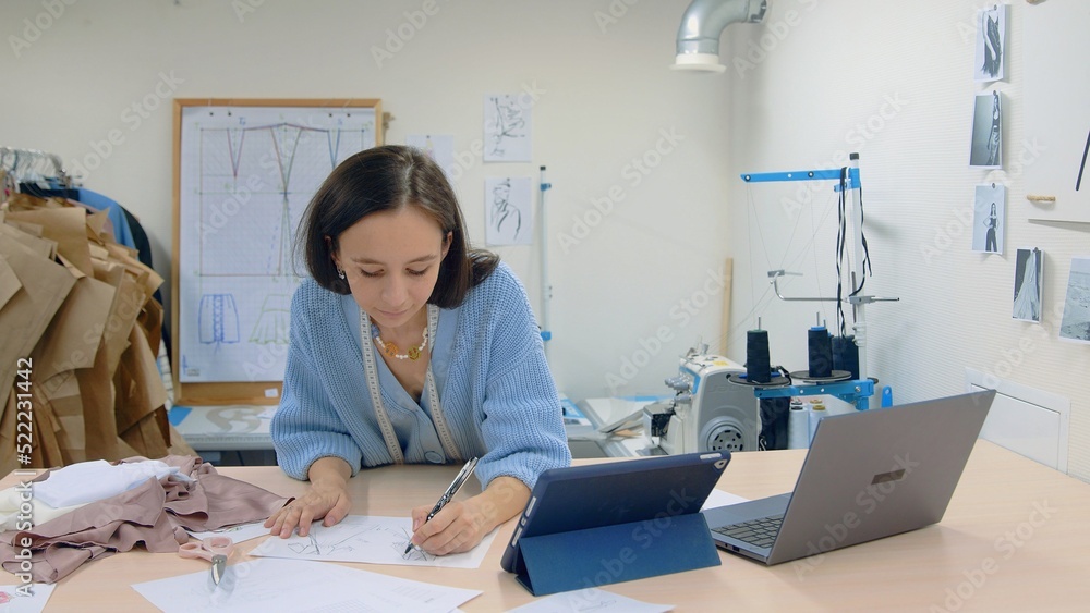 4K. A young woman working in a clothing store. A fashion designer makes sketches on paper. 4K. A young woman working in a clothing store. A fashion designer makes sketches on paper.