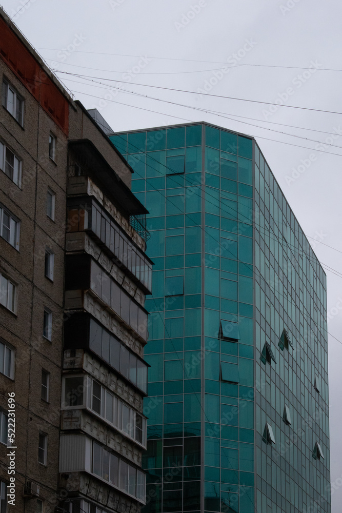 An urban concrete glass office against the background of a typical post-Soviet five-story building in cloudy and rainy weather
