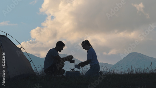 The romantic couple sitting near the campsite tent and preparing tea