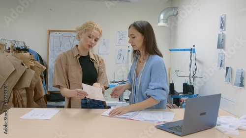 4K. A young female seamstress works with a client in a sewing workshop. They are looking at sketches of dresses