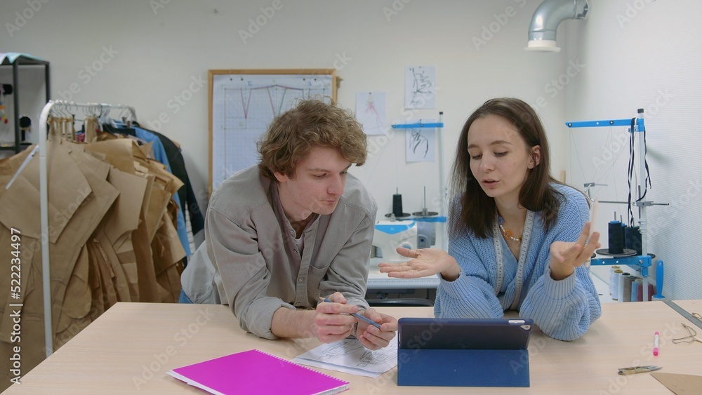 4K. A young female seamstress works with a client in a sewing workshop. They are looking at sketches of dresses 4K. A young female seamstress works with a client in a sewing workshop. They are looking at sketches of dresses