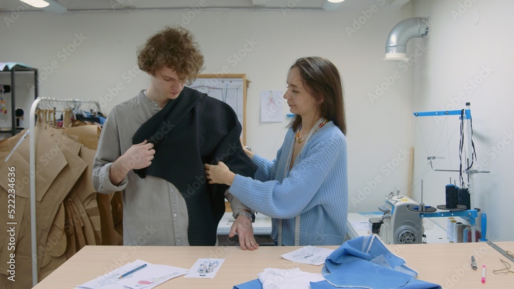 Obraz premium 4K. A young seamstress works with a client in a sewing workshop. They pick up the fabric