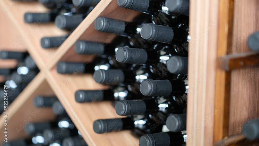 Naklejka premium Red wine bottles stacked on wooden racks closeup
