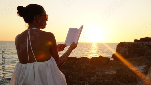 Silhouette of an elegant woman sitting on a rock in front of an idyllic sunset in sardegna italy, she breathes air of changes in her life and reads a book relaxed