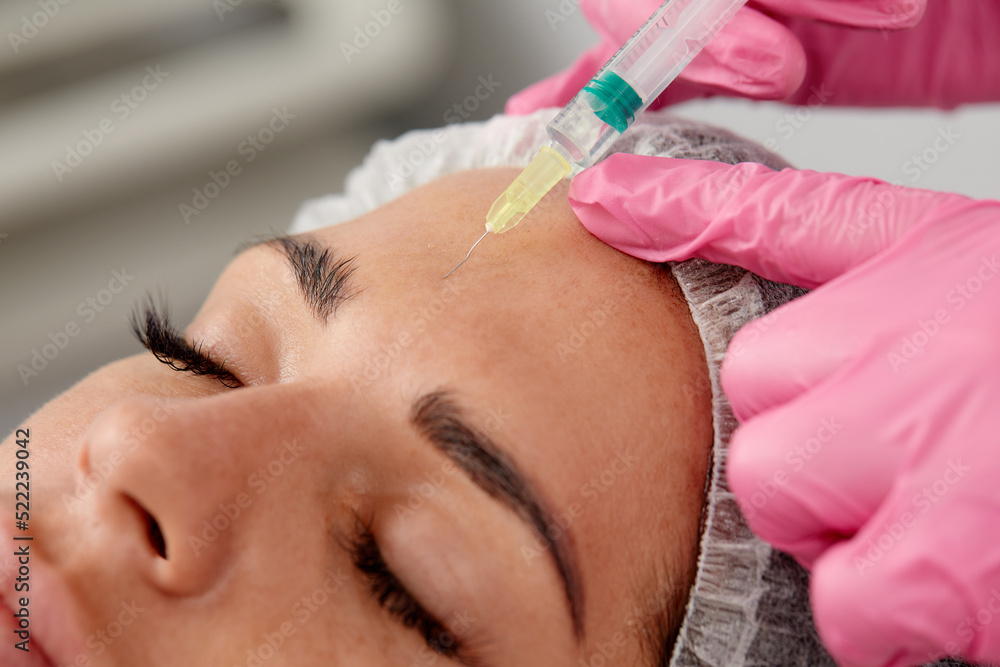Portrait of young Caucasian woman getting botox cosmetic injection in forehead. Beautiful woman gets botox injection in her face Portrait of young Caucasian woman getting botox cosmetic injection in forehead. Beautiful woman gets botox injection in her face