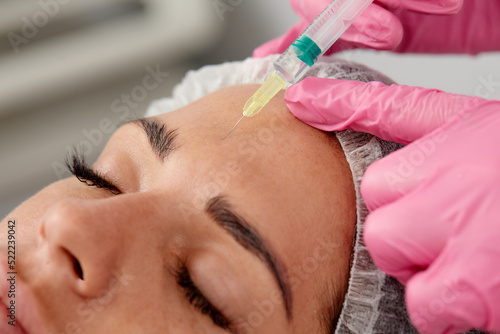 Portrait of young Caucasian woman getting botox cosmetic injection in forehead. Beautiful woman gets botox injection in her face