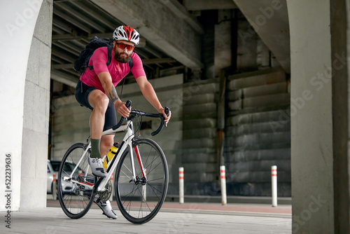 Portrait of a cyclist standing under a bridge with a bicycle, posing at the camera against an architecture background. Active lifestyle. Cycling is a hobby.