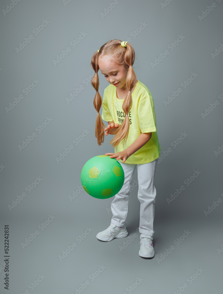 a little girl throws a ball up, isolated on a gray background. a little athlete.children's sports. a little girl throws a ball up, isolated on a gray background. a little athlete.children's sports.