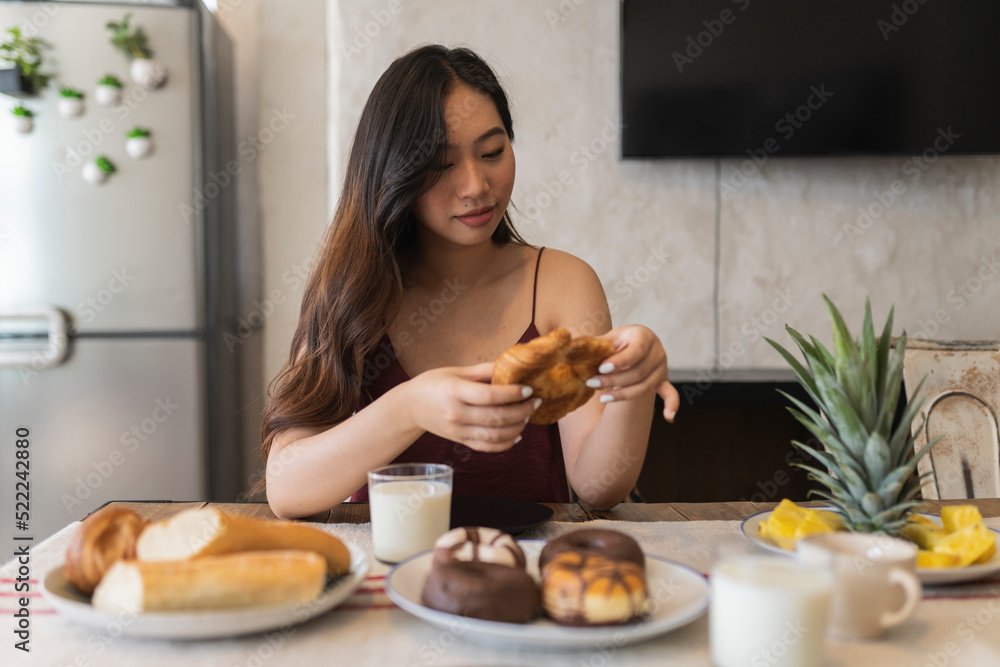 pretty asian woman having croissant breakfast at home