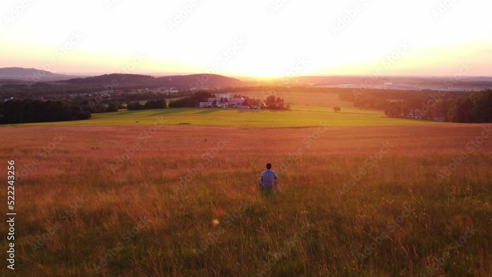 Thoughtful man in a colourful shirt walks in the early evening light through a meadow teeming with life and biodiversity, wondering how to preserve this healthy ecosystem. Thoughtful man in a colourful shirt walks in the early evening light through a meadow teeming with life and biodiversity, wondering how to preserve this healthy ecosystem.