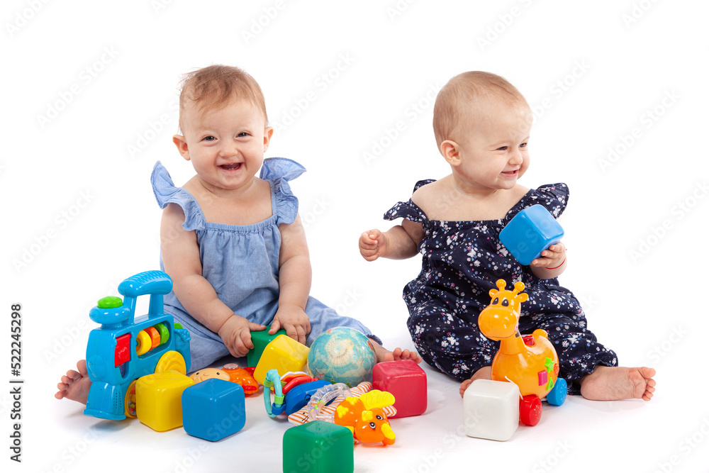 Two cute baby girls playing with toys, isolated on white. Having fun, smiling Two cute baby girls playing with toys, isolated on white. Having fun, smiling