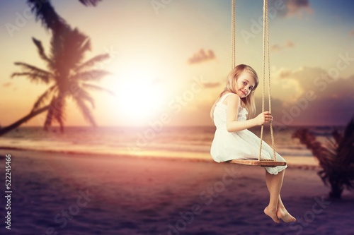 Child tourist swinging on swing, sandy beach. Tropical vacation.