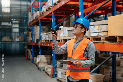 Storage Asian worker in uniform and notepad,digital tablet in hands checks production. warehouse concept..