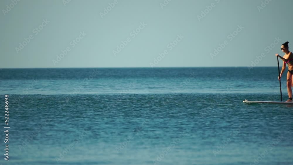 Sea woman sup. Silhouette of happy middle aged woman in rainbow bikini, surfing on SUP board, confident paddling through water surface. Idyllic sunset. Active lifestyle at sea or river. Slow motion Sea woman sup. Silhouette of happy middle aged woman in rainbow bikini, surfing on SUP board, confident paddling through water surface. Idyllic sunset. Active lifestyle at sea or river. Slow motion